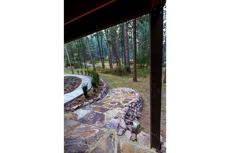 A short ramp leads to a forested yard. The ramp is lined with large rocks, and is made from paving stones set in concrete.